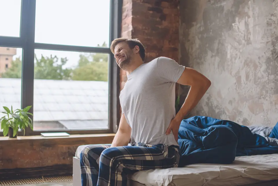 Homme assis au bord du lit, la main sur le bas du dos
