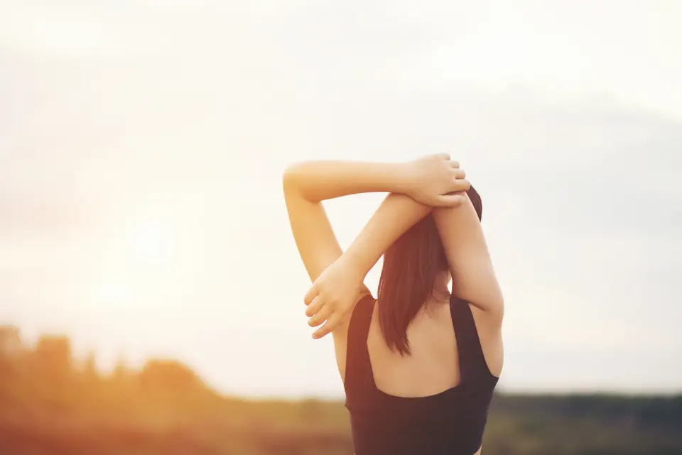 Femme de dos qui étire ses épaules, les bras croisés derrière la tête