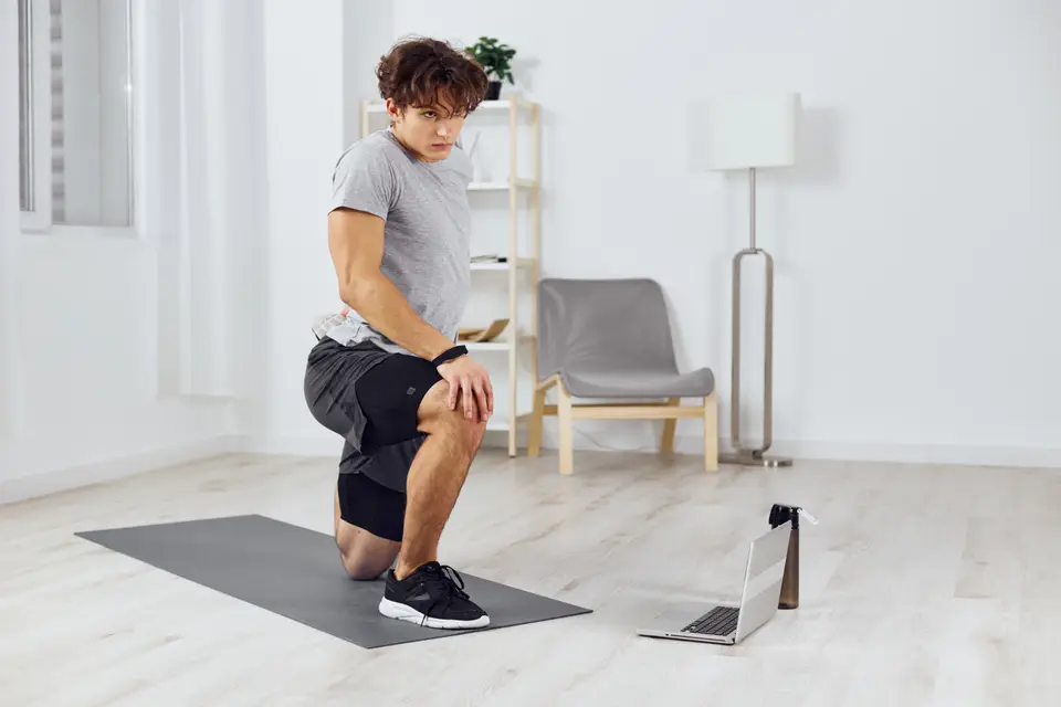 Homme qui fait un exercice de mobilité du genou sur un tapis, devant un ordinateur